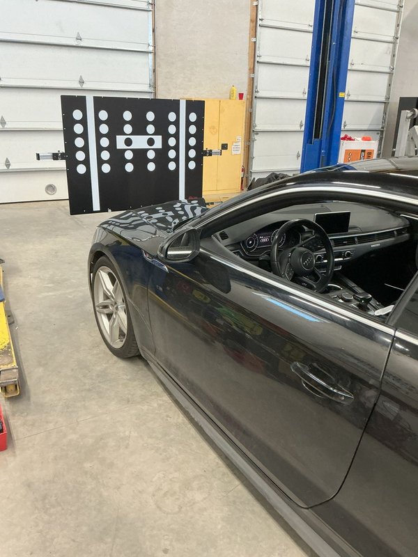ADAS calibration target board set up in front of a dark sedan in the Shattered Vision shop, Colorado Springs