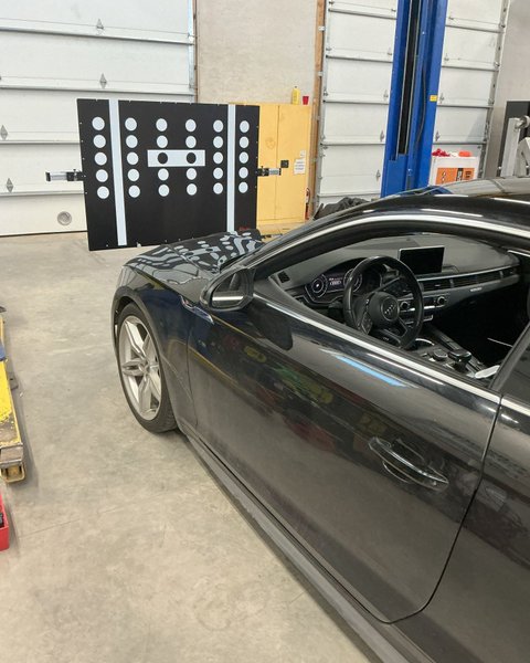 ADAS calibration target board set up in front of a dark sedan in the Shattered Vision shop, Colorado Springs